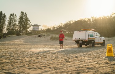 A surf life saver standing on the beach piloting a drone